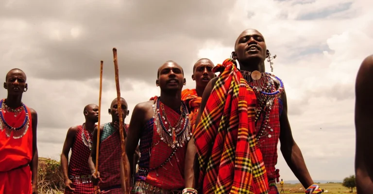 Maasai men in red and checked shukas and beaded collars sing and jump during a traditional dance
