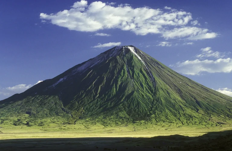 The steep grey-green cone of Ol Doinyo Lengai rises from the flat plains under white clouds