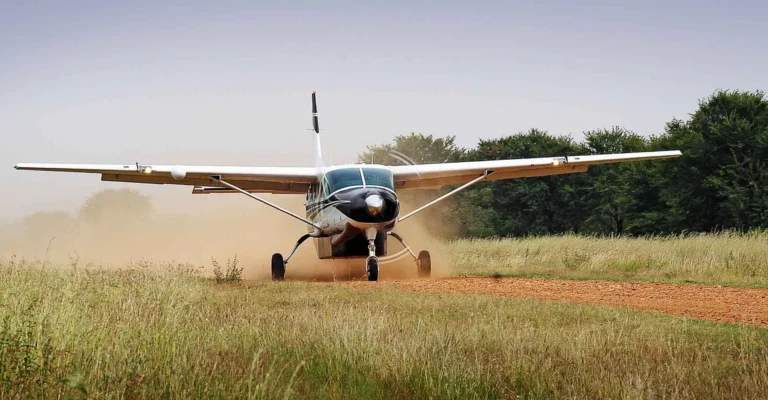 A single-engine bush plane taxis along a grass and dirt airstrip, kicking up dust