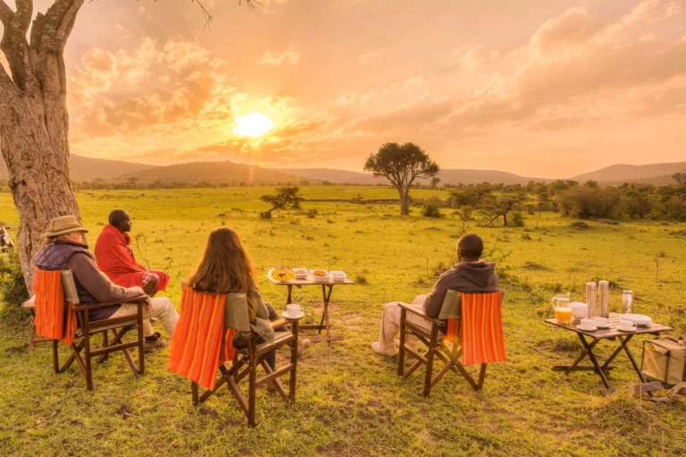 Travellers eat breakfast at camp tables on the open plains as the sun rises