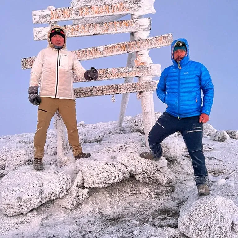 Two climbers at the Uhuru Peak summit sign on Kilimanjaro