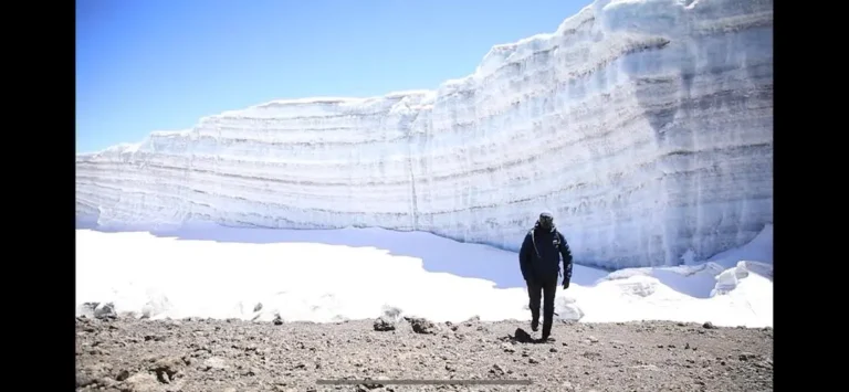 A climber walks beneath the layered ice wall of a glacier near the summit of Kilimanjaro