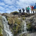 Climbers wave from rocks above a small waterfall in Kilimanjaro's moorland zone