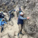 Climbers scramble along a rocky section of trail, hands on the rock, as on the Barranco Wall