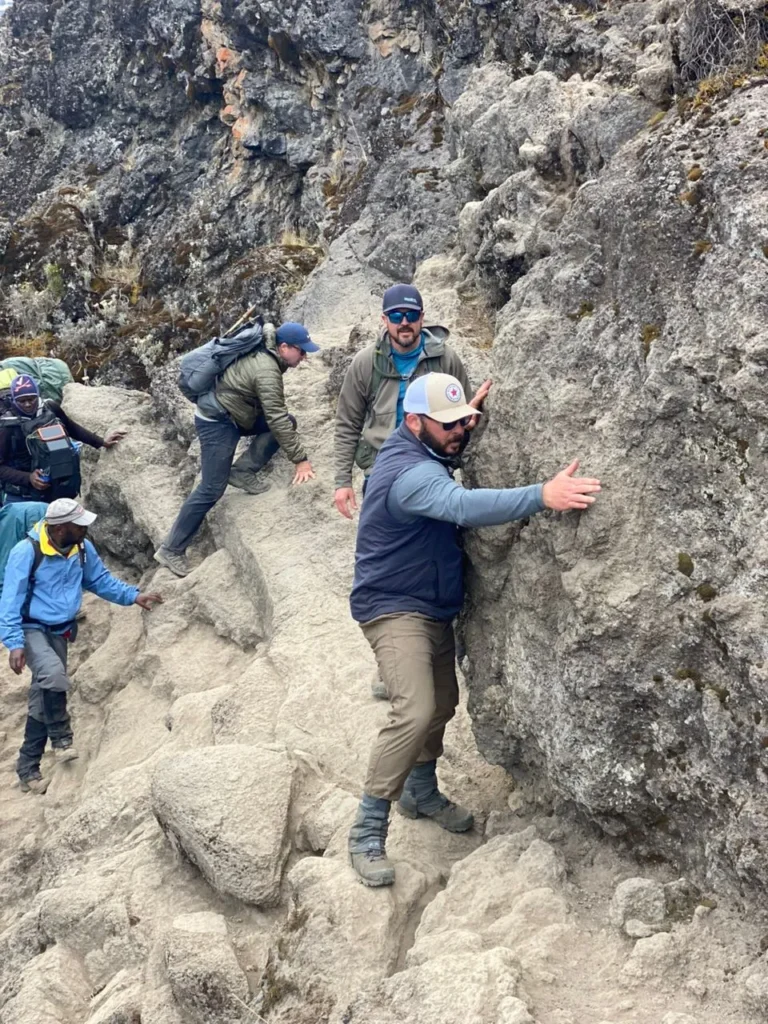 Climbers scramble along a rocky section of trail, hands on the rock, as on the Barranco Wall