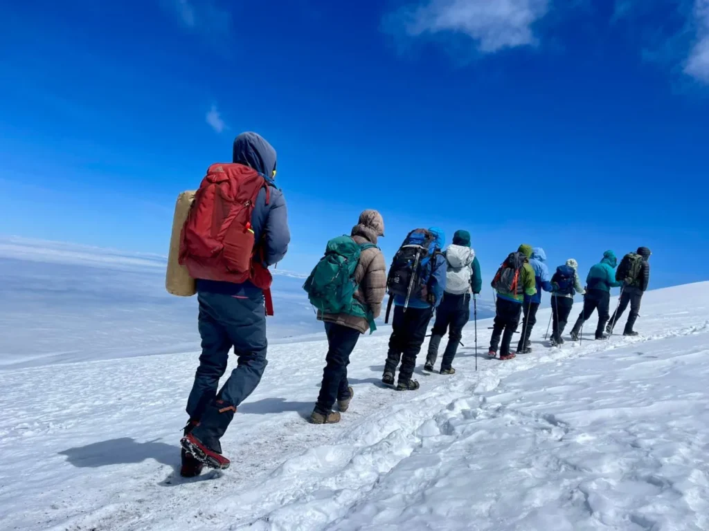 Climbers with backpacks and trekking poles cross fresh snow high on Kilimanjaro under a deep blue sky