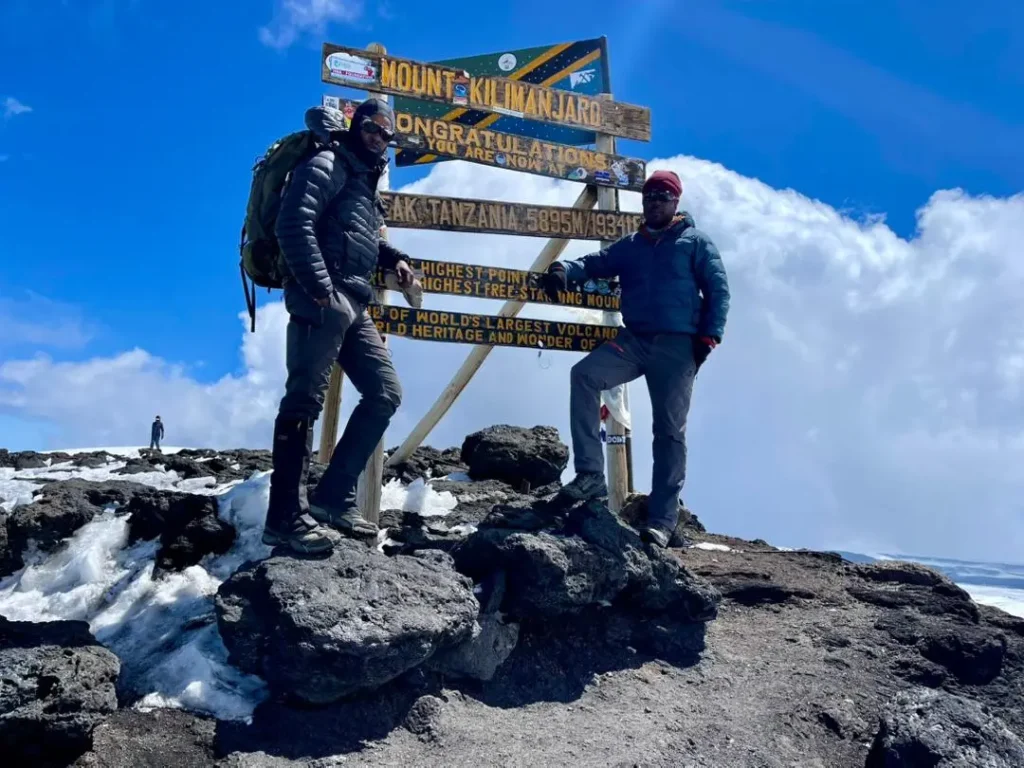 Two climbers celebrate beside the summit signboard at Uhuru Peak, Kilimanjaro